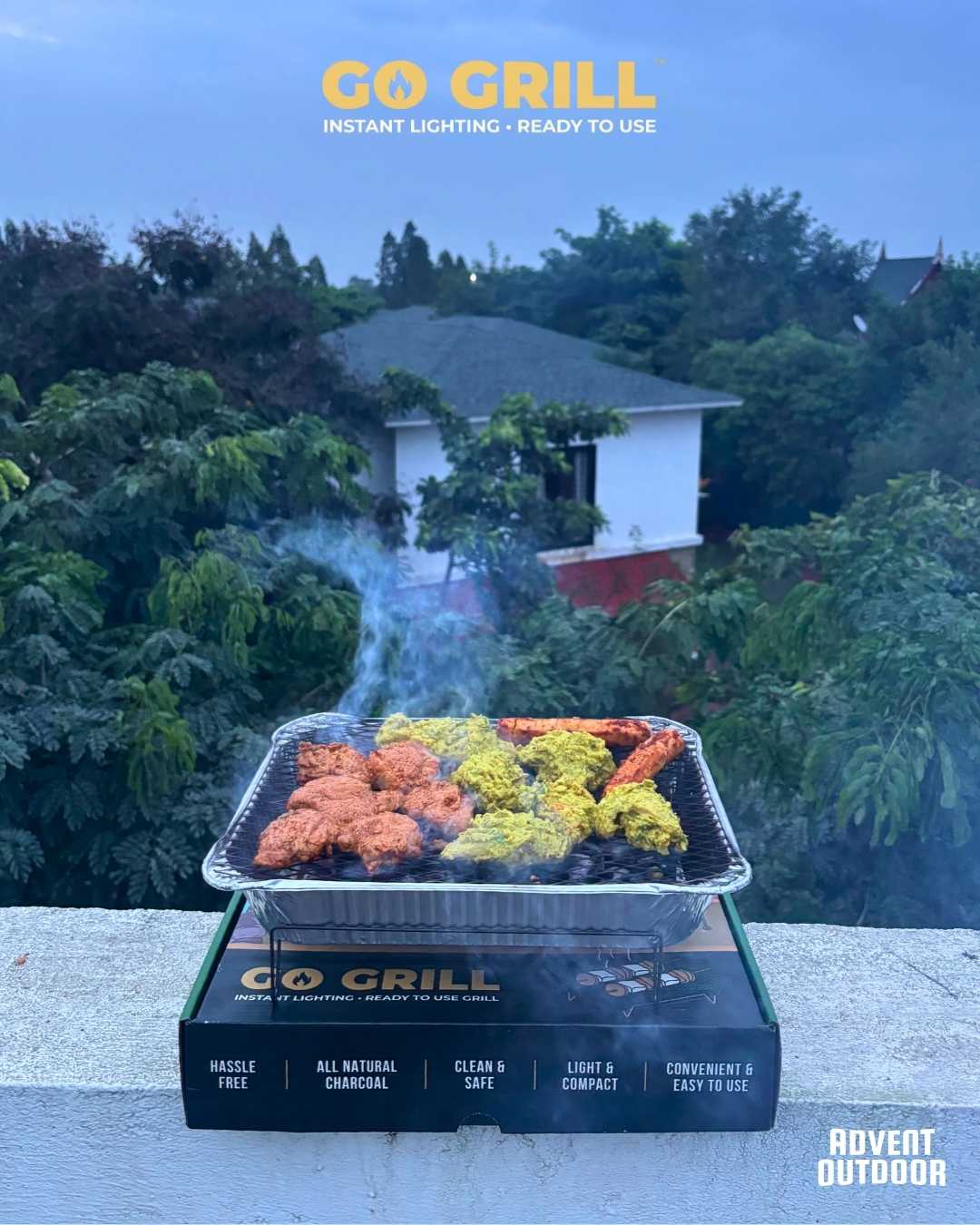Go Grill disposable BBQ placed on its box, grilling assorted marinated tikkas on a terrace with a lush green view — perfect for rooftop BBQ sessions.