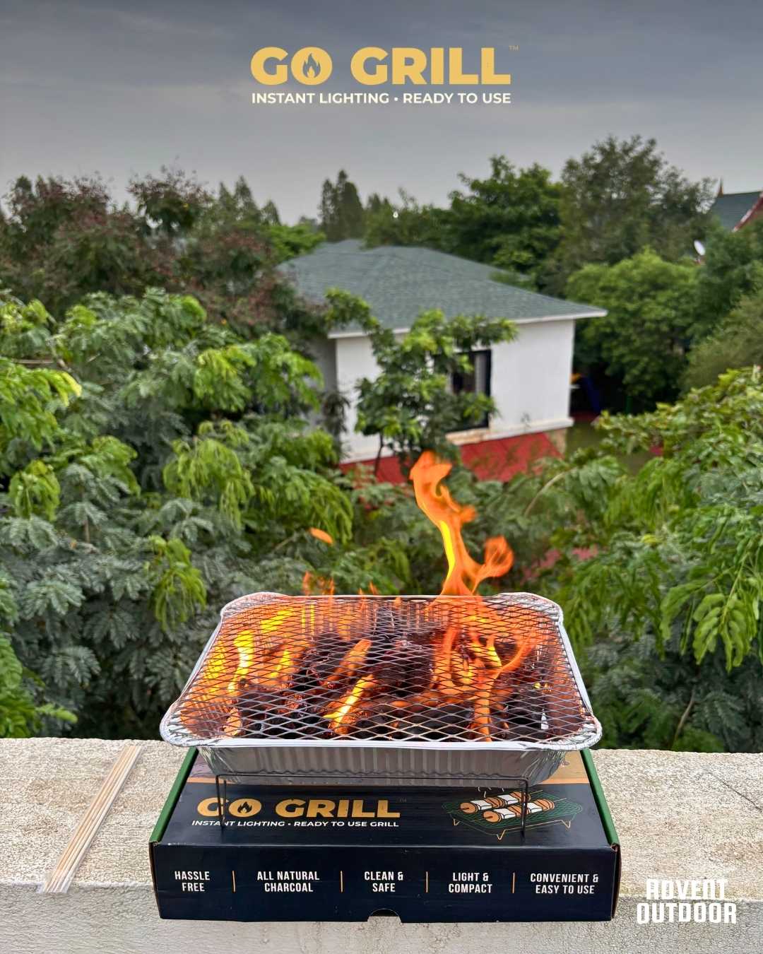 Go Grill disposable BBQ with flames rising during ignition, placed on its box against a green rooftop backdrop — ideal for quick outdoor grilling.