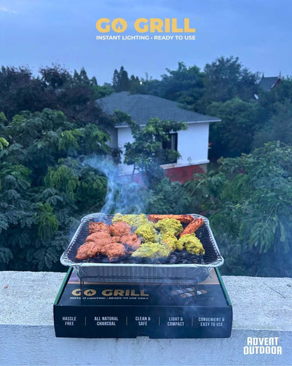 Go Grill disposable BBQ placed on its box, grilling assorted marinated tikkas on a terrace with a lush green view — perfect for rooftop BBQ sessions.